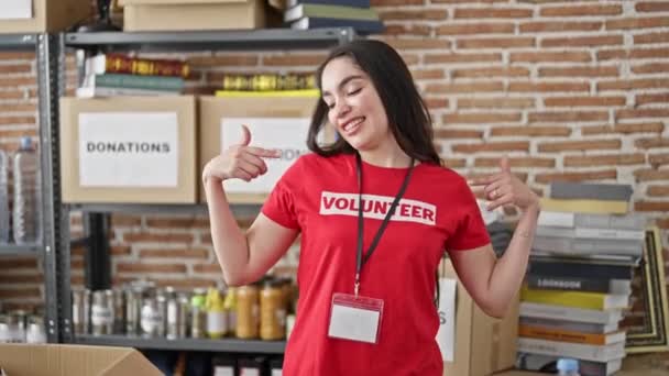 チャリティセンターでボランティア制服の笑顔を指す若い美しいヒスパニック女性 — ストック動画