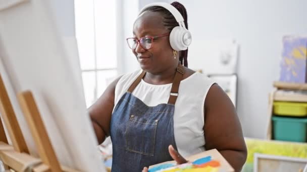 自信を持ったアフリカ系アメリカ人女性アーティストが情熱を持って描き アートスタジオで音楽を聴き 曲線を抱き 笑顔で — ストック動画