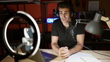 Bir radyo programında konuşan İspanyol genç adam radyo stüdyosunda akıllı telefondan video kaydediyor.