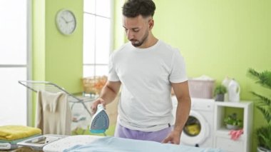 Çamaşır odasında gömlek tutan genç bir Arap ütü yapıyor.