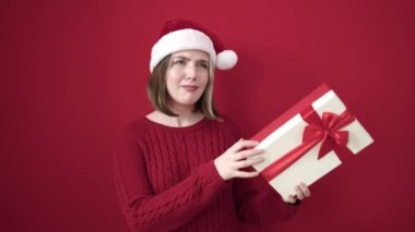 Genç sarışın kadın Noel şapkası takıyor hediye duyma sesi izole edilmiş kırmızı arka planda.