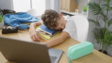 Sevimli sarışın çocuk, yorgun ama çalışkan, rahat bir sınıfta ders kitaplarının üzerinde uyurken yakalandı.