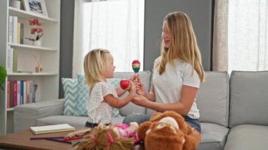 Kendinden emin beyaz anne ve küçük kızı, neşeli bir ikili, marakas çalıyorlar, evde birlikte dans ediyorlar, gülüşleri oturma odasını aydınlatıyor..