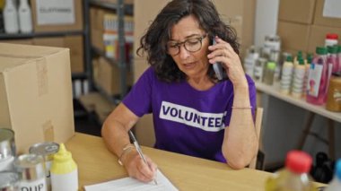 Orta yaşlı İspanyol kadın yardım merkezinde akıllı telefondan konuşan bir belgeye gönüllü olarak yazı yazıyor.