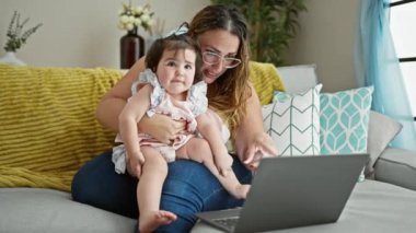 Anne ve kızının gülümseme anı, evdeki dizüstü bilgisayarla bir aile video görüşmesi yaparken koltukta dinlenmek. Anne sevgisi gözlerinde kendini ifade eder..