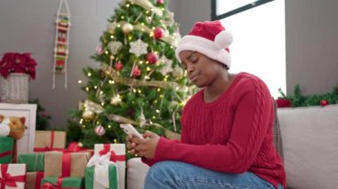 Afrika kökenli Amerikalı bir kadın Noel 'i evde stresli bir ifadeyle akıllı telefon kullanarak kutluyor.