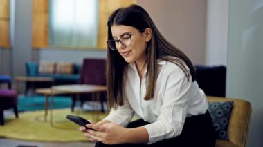 Ofisteki sandalyede oturan, akıllı telefon kullanan genç, güzel İspanyol kadın.