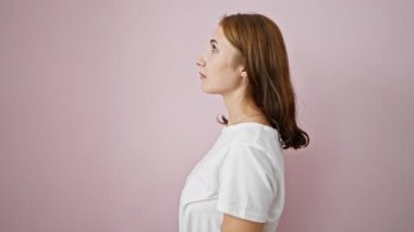 Soyutlanmış pembe arka planda sürpriz bir ifadeyle duran genç bir kadın.
