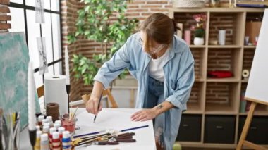 Sanat stüdyosunda duran genç kadın ressam kağıt üzerine resim çiziyor.