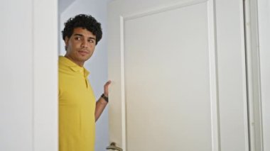 Üzgün yüzlü genç latin adam evinin kapısını kapatıyor.