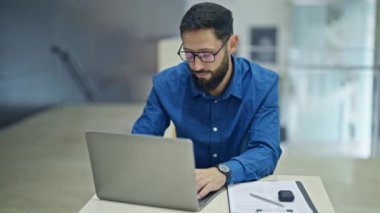 Genç İspanyol iş adamı ofiste gözlüğünü çıkarırken dizüstü bilgisayar kullanıyor.