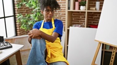 African american woman artist smiling confident sitting on chair at art studio
