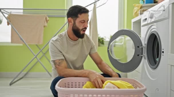 年轻人在洗衣房洗衣服时看起来很不高兴 — 图库视频影像