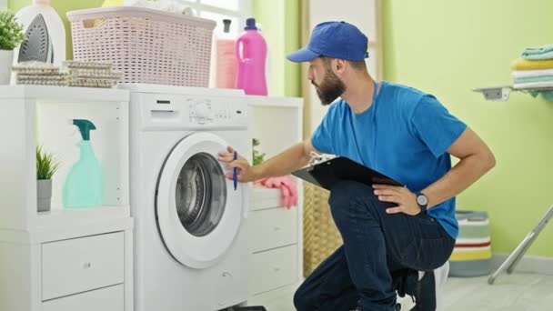 Jovem Hispânico Técnico Reparando Máquina Lavar Roupa Escrita Relatório Lavanderia — Vídeo de Stock