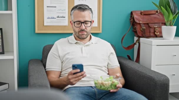 Grijsharige Man Zakelijke Werknemer Met Behulp Van Smartphone Eten Salade — Stockvideo