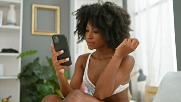 アフリカ系アメリカ人女性 ベッドに座ってスマートフォンを使用して ベッドルームでセクシーに見える — ストック動画