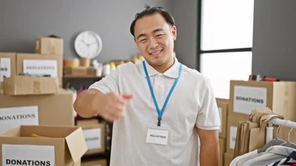 笑顔で自信に満ちた若い中国人男性は 心温まるチャリティセンターでボランティアをしている間 ジェスチャーに完全に親指を与えます — ストック動画