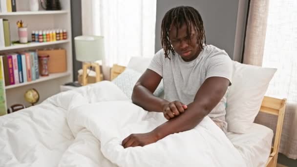 アフリカ系アメリカ人男性は寝室でベッドに座っているかゆみのあるために腕を掻く — ストック動画