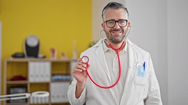 Grauhaariger Arzt Lächelt Zuversichtlich Und Hält Stethoskop Der Klinik — Stockvideo