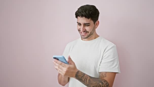 年轻的惊慌失措的男人用智能手机对着孤立的粉色背景微笑 — 图库视频影像