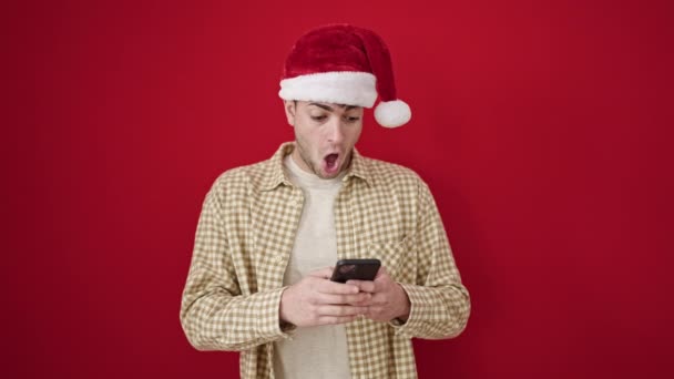 Jonge Spaanse Man Draagt Kerst Hoed Wijzend Naar Smartphone Geïsoleerde — Stockvideo
