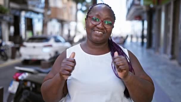 自信的非洲裔美国女人在阳光灿烂的城市街道上闪烁着一个有趣的 认可的竖起大拇指的标志 她那凉爽的眼镜闪烁着光芒 — 图库视频影像