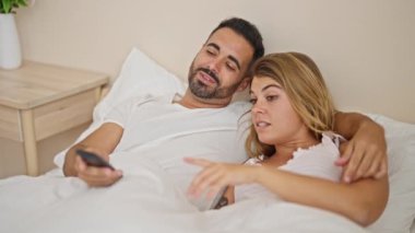 Kadın ve erkek yatak odasında uzanmış televizyon seyrediyor.