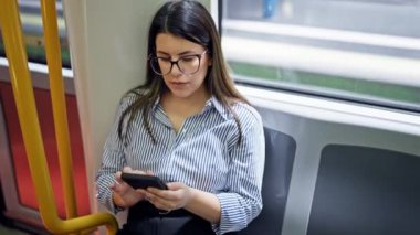 Genç ve güzel İspanyol kadın metroda oturmuş akıllı telefon kullanıyor.