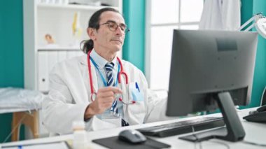 Orta yaşlı doktor klinikte kollarını açarken gözlük takıyor.
