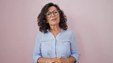 Orta yaşlı İspanyol kadın, kendine güvenen, soyutlanmış pembe arka planda konuşan.