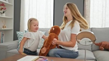 Beyaz tenli anne ve küçük kızı evdeki oturma odasındaki kanepede rahatça dinleniyor ve tatlı oyuncak bebeklerini tararken birlikte değerli bir anı paylaşıyorlar..