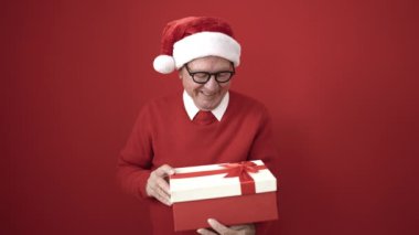 Sunbae, Noel şapkası takıp kırmızı arka planda hediyeleri açıyor.