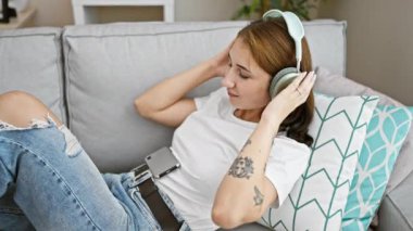 Müzik dinleyen genç bir kadın evdeki kanepede dans ediyor.