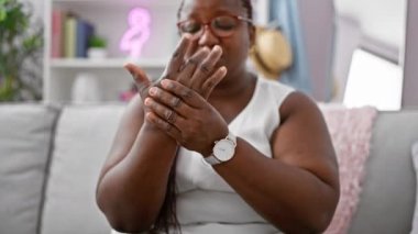 Afro-Amerikalı bir kadın, rahat oturma odasında mutsuz, kanepede oturuyor, ısrarcı el ağrısı konusunda ciddi şekilde endişeli.