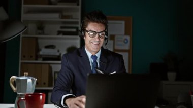 Genç İspanyol iş adamı ofiste kutlama yapmak için dizüstü bilgisayar ve kulaklık kullanıyor.