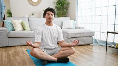 Genç latin adam evde yerde oturup yoga eğitimi alıyor.