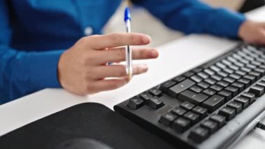 Genç İspanyol iş adamı ofiste elinde kalemle bilgisayar kullanıyor.
