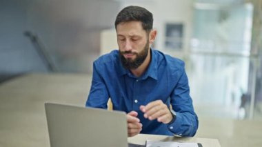Genç İspanyol iş adamı akıllı telefon ve dizüstü bilgisayar kullanıyor. Ofiste stresli.