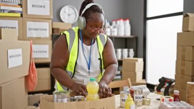 Canlı bir Afro-Amerikan kadını, fedakar bir gönüllü, müziğe ayak uyduruyor, toplum merkezindeki bağış için karton bir kutuya yiyecek dolduruyor.