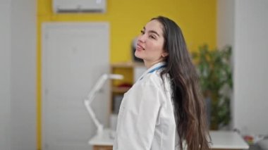 Genç, güzel İspanyol kadın doktor gülümsüyor. Kollarını kavuşturup klinikte kendine güveniyor.