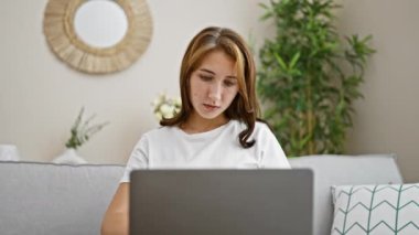 Laptop ve kredi kartıyla alışveriş yapan genç bir kadın evdeki kanepede oturuyor.