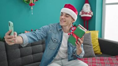 Genç İspanyol adam evde Noel hediyesi tutarak selfie çekiyor.
