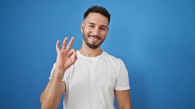 Genç Arap adam gülümsüyor. Kendine güveniyor. İzole edilmiş mavi arkaplanı imzala.