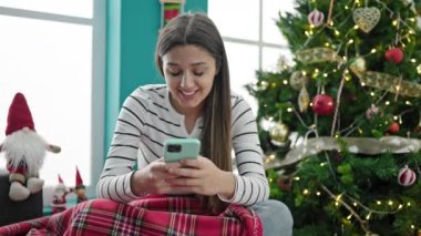 Genç ve güzel İspanyol kadın akıllı telefon kullanarak Noel 'i evde kutluyor.