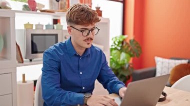 Laptop ve kredi kartıyla alışveriş yapan İspanyol genç adam yemek odasında masada oturuyor.