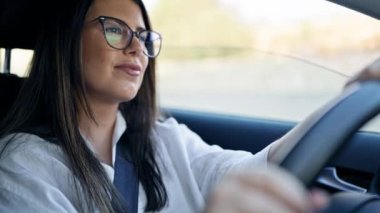 Genç, güzel, İspanyol bir kadın. Araba kullanıyor. Gözlüklü, gülümsüyor.