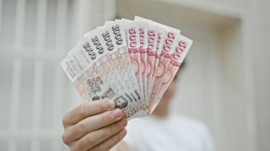 Neşeli, genç İspanyol genç kendine güvenen bir tomar İzlanda Krona banknotunu, hareketli bir şehir caddesinde göz kamaştırıcı bir tebessümle sergiliyor.