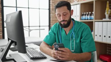 Genç İspanyol doktor klinikte rahatlarken akıllı telefon kullanıyor.