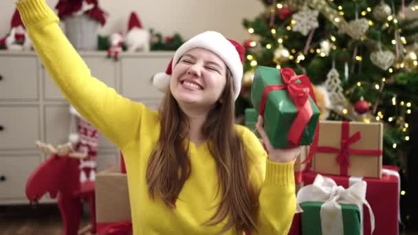 年轻的金发女郎 手里拿着礼物 坐在家里的圣诞树旁 — 图库视频影像
