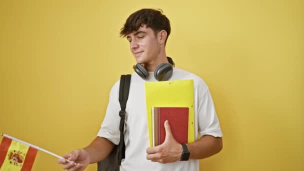 年轻自信的他的恐慌少年 一个聪明的学生 带着他的书 在一个充满活力的黄色孤立的背景下炫耀西班牙国旗 — 图库视频影像